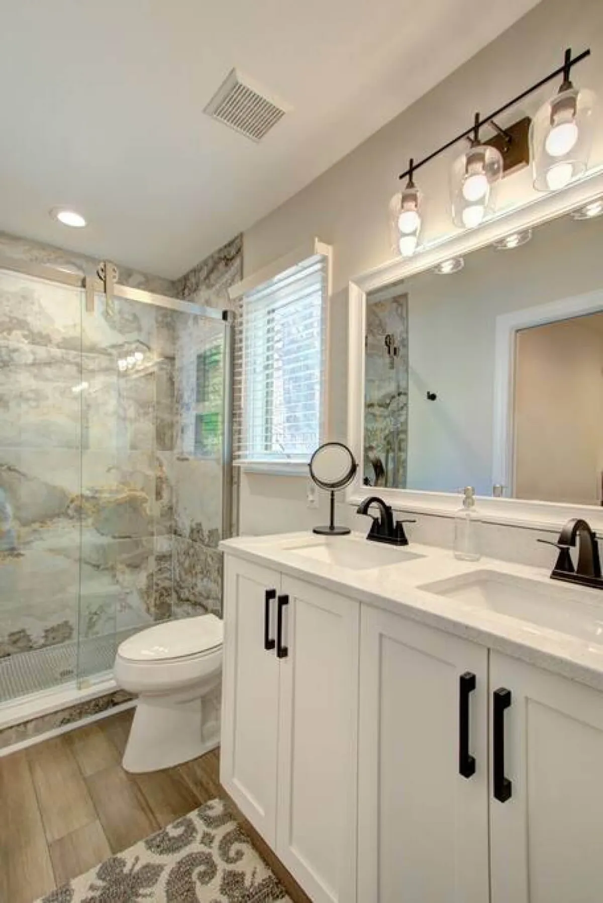 A modern bathroom with a double sink vanity, glass shower enclosure, decorative mirror, and stylish lighting. The space is fresh and spa-like, perfect for morning routines or unwinding after a lakeside adventure.