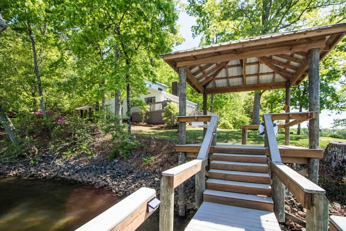 A peaceful lakeside scene with a dock extending over the water, a charming gazebo nearby, and lush greenery all around. The space feels open and welcoming, ideal for fishing, picnicking, or watching the sunset.