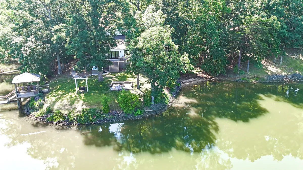 A wide exterior view featuring the house, private dock, glistening water, shaded trees, and a charming gazebo. The image captures both the dock and the inviting waterfront area, as well as space for activities like fishing, boating, or relaxing by the lake.